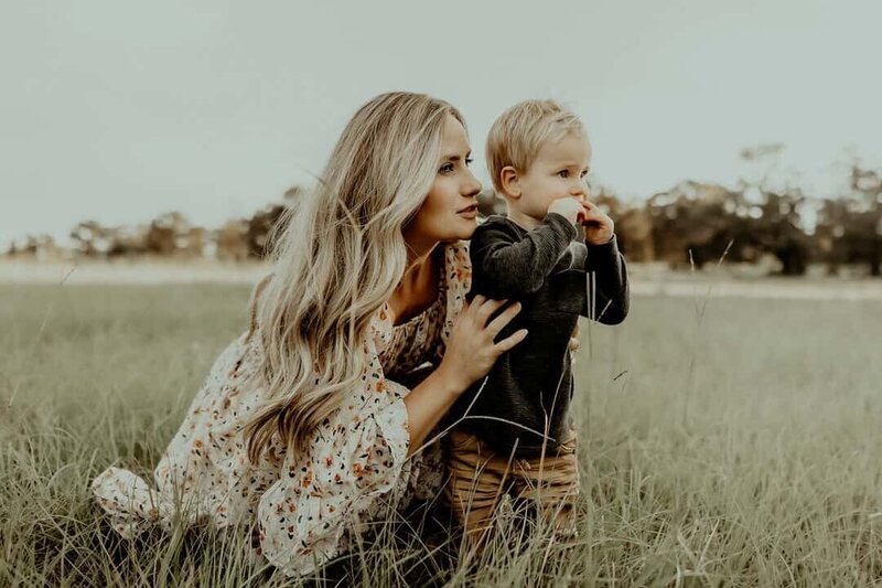 A woman kneels beside a young child in a grassy field, both looking into the distance a perfect moment captured by a skilled Warner Robins Family photographer.