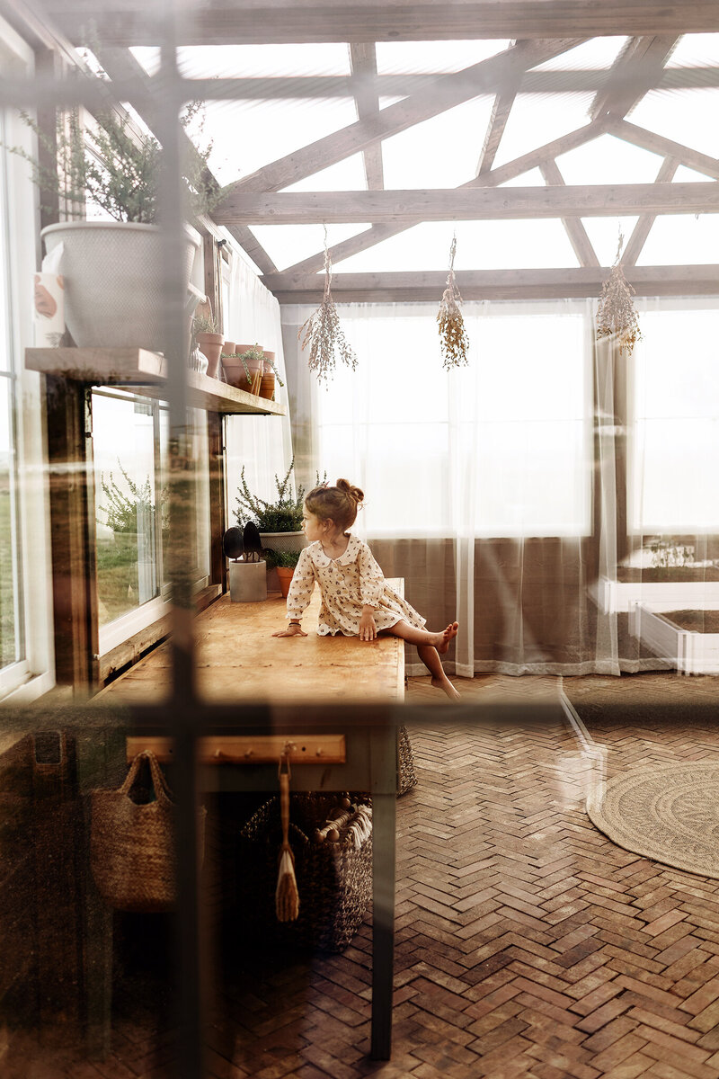 little girl peering out the window in a greenhouse in fort collins, colorado