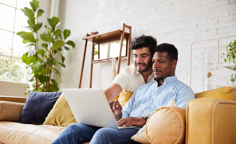 Diverse male couple looking at laptop together.