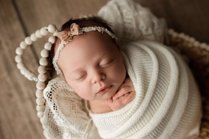 newborn baby girl wrapped in a soft peach wrap with her toes poking out and a tiny pink bow on a newborn bed during newborn session in harrisburg pa