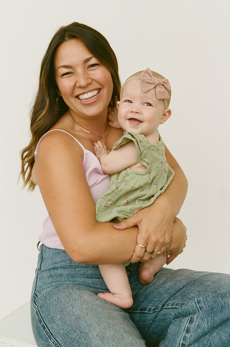 A close up photo of Brooklyn family and newborn photographer, Samantha Okazaki. She's wearing a blue denim shirt and is smiling brightly right at the camera.