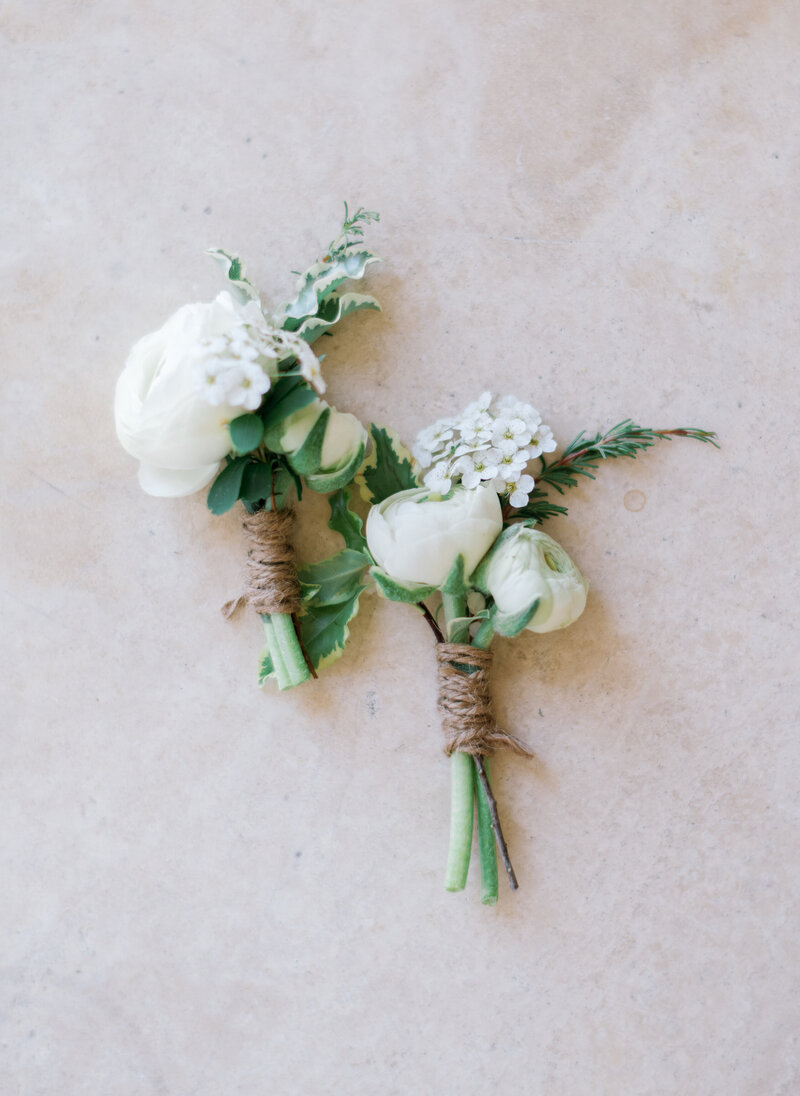 2 Boutonnieres with fresh white flowers and greenery on cream background