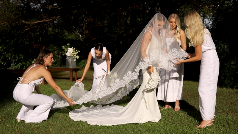 A new bride stands as her bridesmaids fix her long wedding veil
