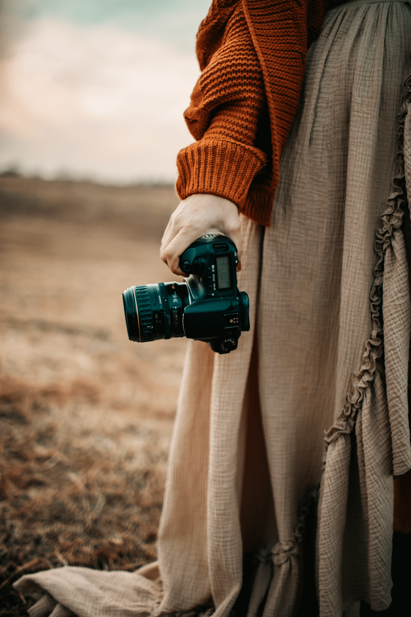 Woman wearing brown dress holding camera in open field