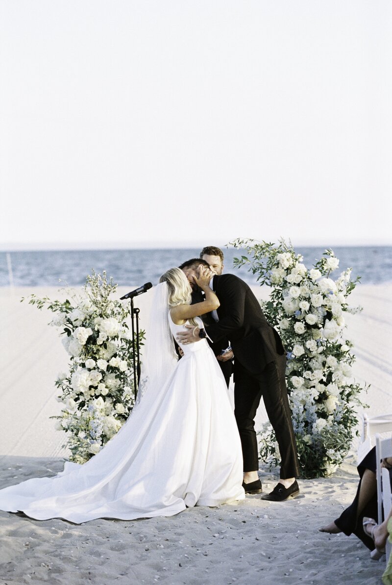 first kiss of bride and groom at sunset on the beach during the wedding ceremony at  Wychmere Beach Club Cape Cod Wedding