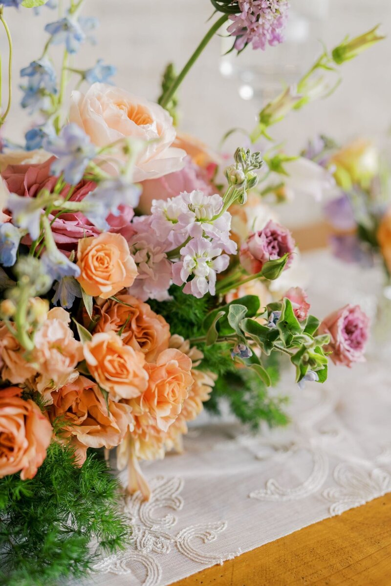 Romantic pastel wedding centerpiece with garden roses, ranunculus, and lush greenery on pink linen table