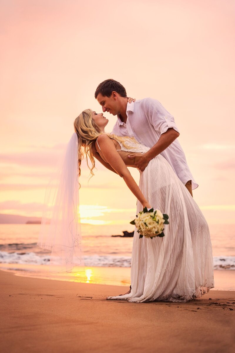 A groom gently dips his bride on the beach at sunset after their elopement in Galveston, Texas.