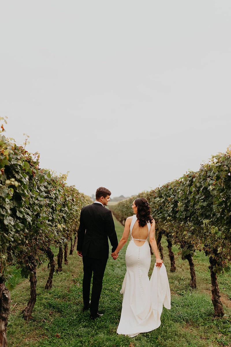 The bride and groom stroll hand in hand along a vineyard pathway, creating a picturesque moment at the winery.