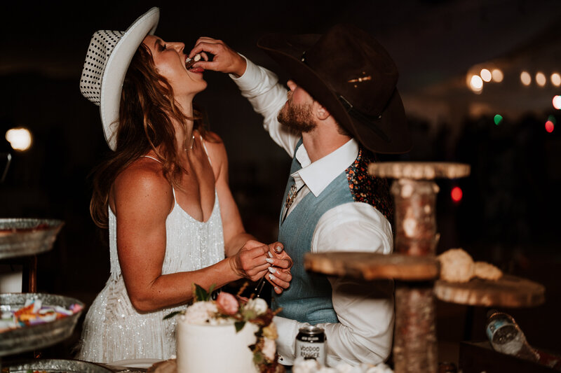 Bride laughs while groom feeds her cake at rustic Breckenridge wedding, captured by photo video duo.