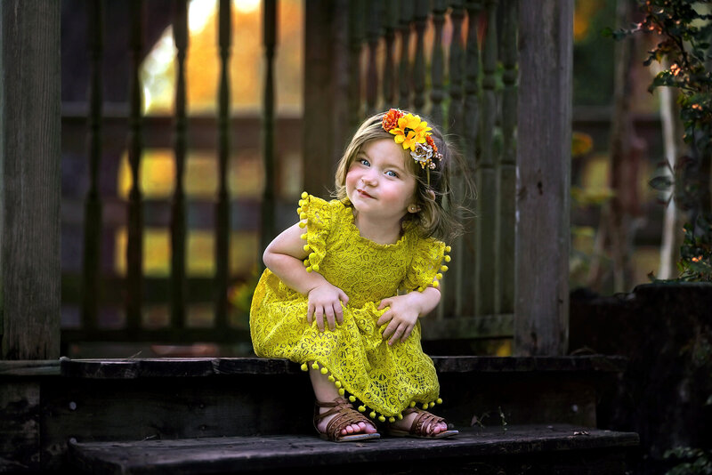 Adorable little girl wearing a yellow dress smiling at the camera.