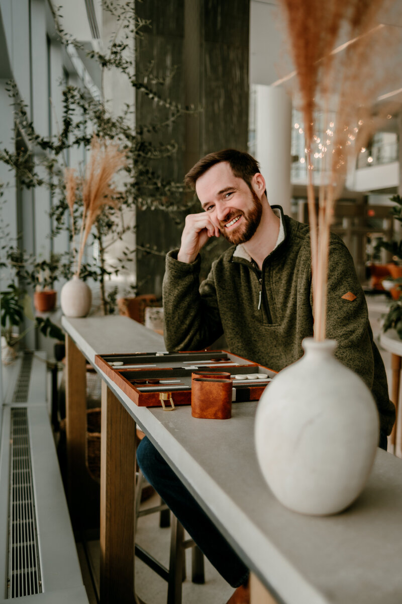 A man smiling during an online dating portrait session in a modern indoor setting in Minneapolis. Captured by Shannon Kathleen Photography, specializing in on-location dating profile photography.