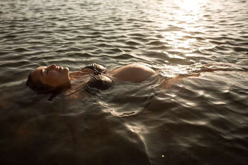 A pregnant mother floats in the water for a sunrise outdoor beach photoshoot on a gold coast beach. She is peaceful and her pregnat belly is softly lit but the rising sun. Photo by Maternity Photographer - Rebecca Rottcher