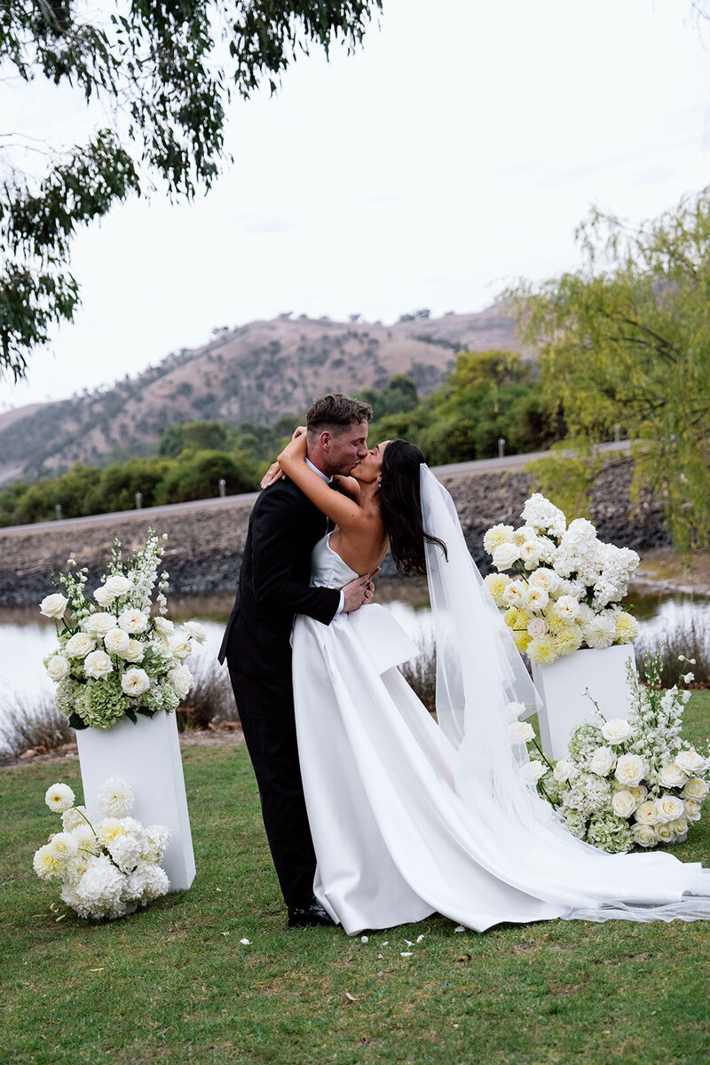 Bride and groom at ceremony on white stage under trees