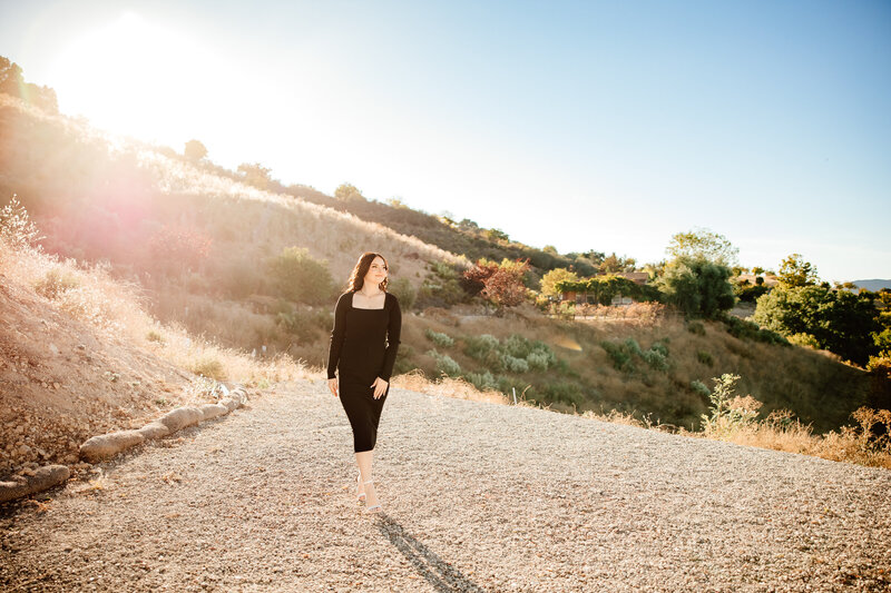 Senior girl walking against beautiful sunlit green hills backdrop
