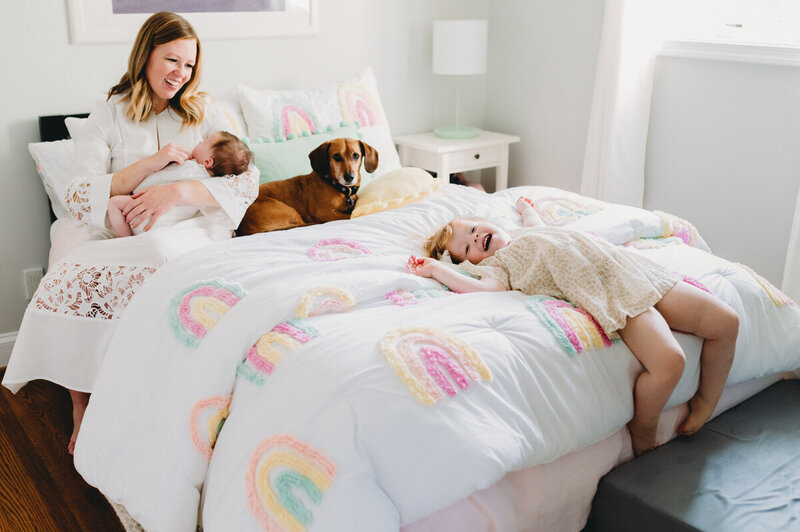 mom with baby and dog sitting on bed with little girl playing