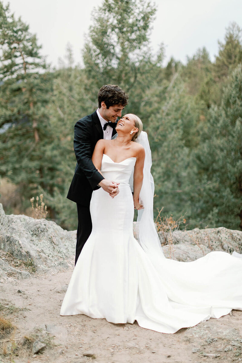 Bride and groom kissing under wedding veil while holding bridal bouquet of flowers
