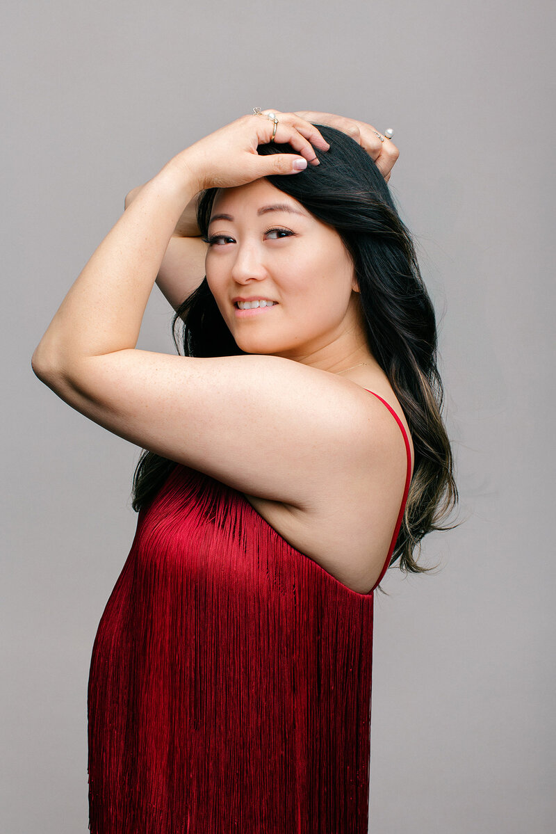 wearing a red dress and arms artfully raised and embracing the top of her head
