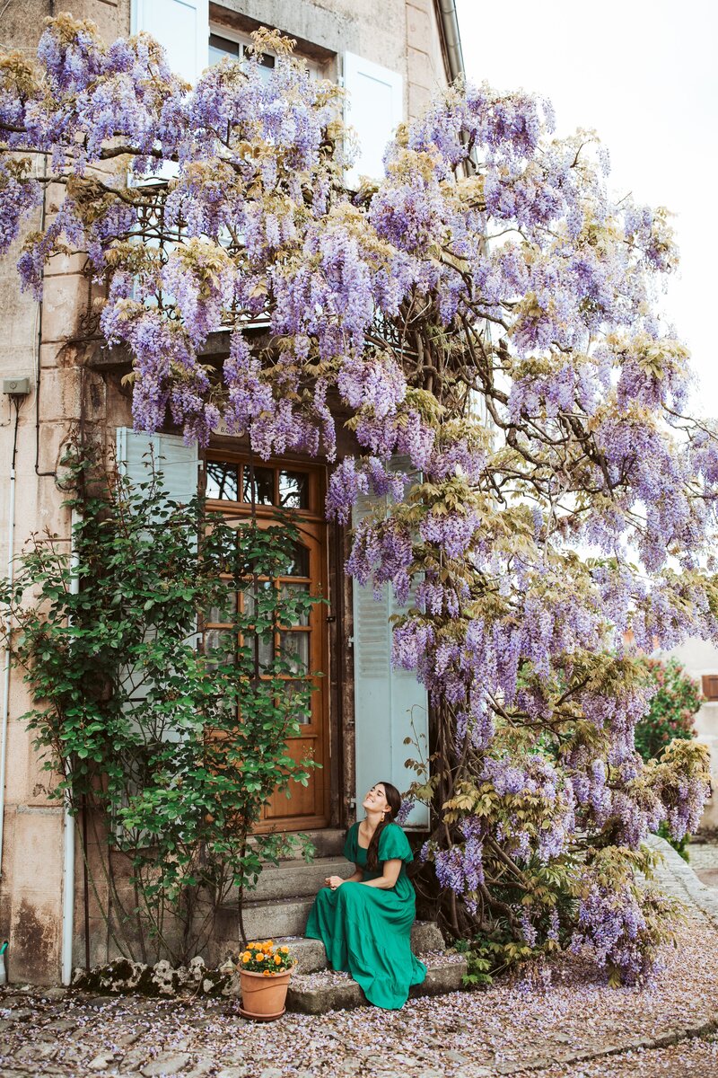 Katie Arnold, Portland Maine wedding photographer, sitting on a doorstep in France underneath flowers.