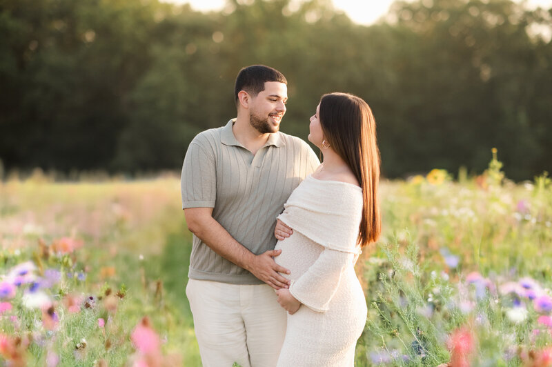 expecting couple holding each other in a flower field near Lancaster, PA during golden hour