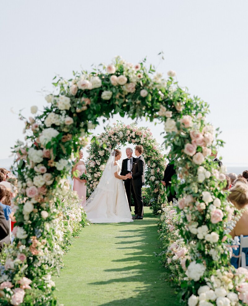 Rachael and Joseph's lush wedding ceremony adorned with floral arches. Discover Bliss Productions—a premier full-service wedding and event design company based in Laguna Beach, California. Every project we design reflects our passion for artistry and precision, turning visions into bespoke celebrations that leave a lasting impression. With decades of combined expertise in event planning, interior design, and branding, we transform every detail into an unforgettable experience that captures the unique vision and style of our clients.