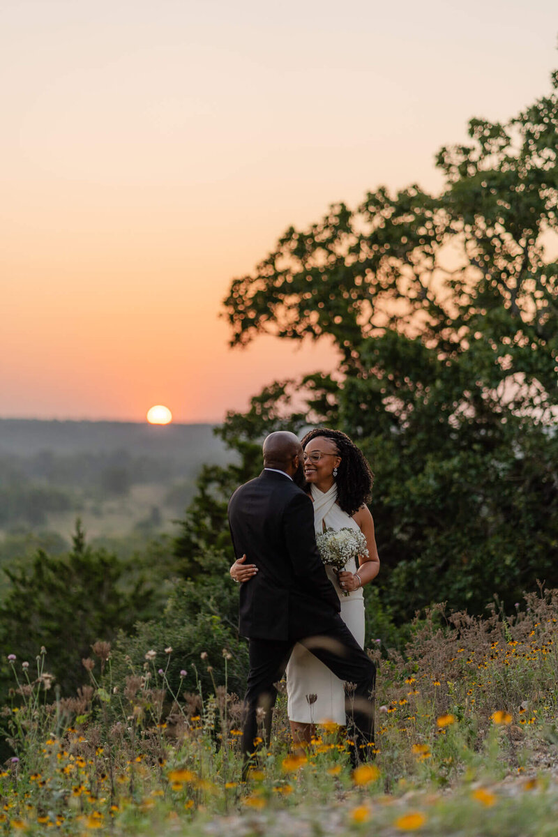couple standing in the wildflowers at an overlook as the sun goes down