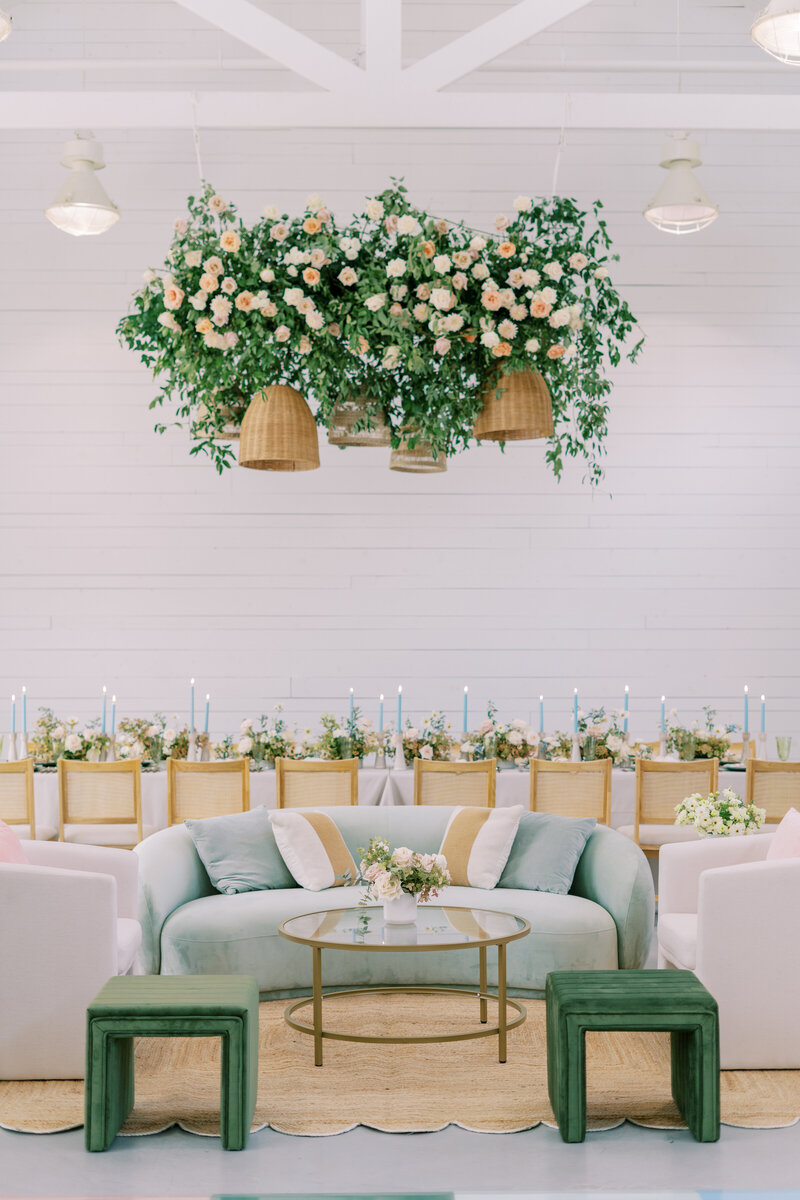 Elegant wedding lounge with mint velvet sofa, rattan pendant lights, and floral ceiling installation above modern reception tables, designed by Eventive Designs in Austin.
