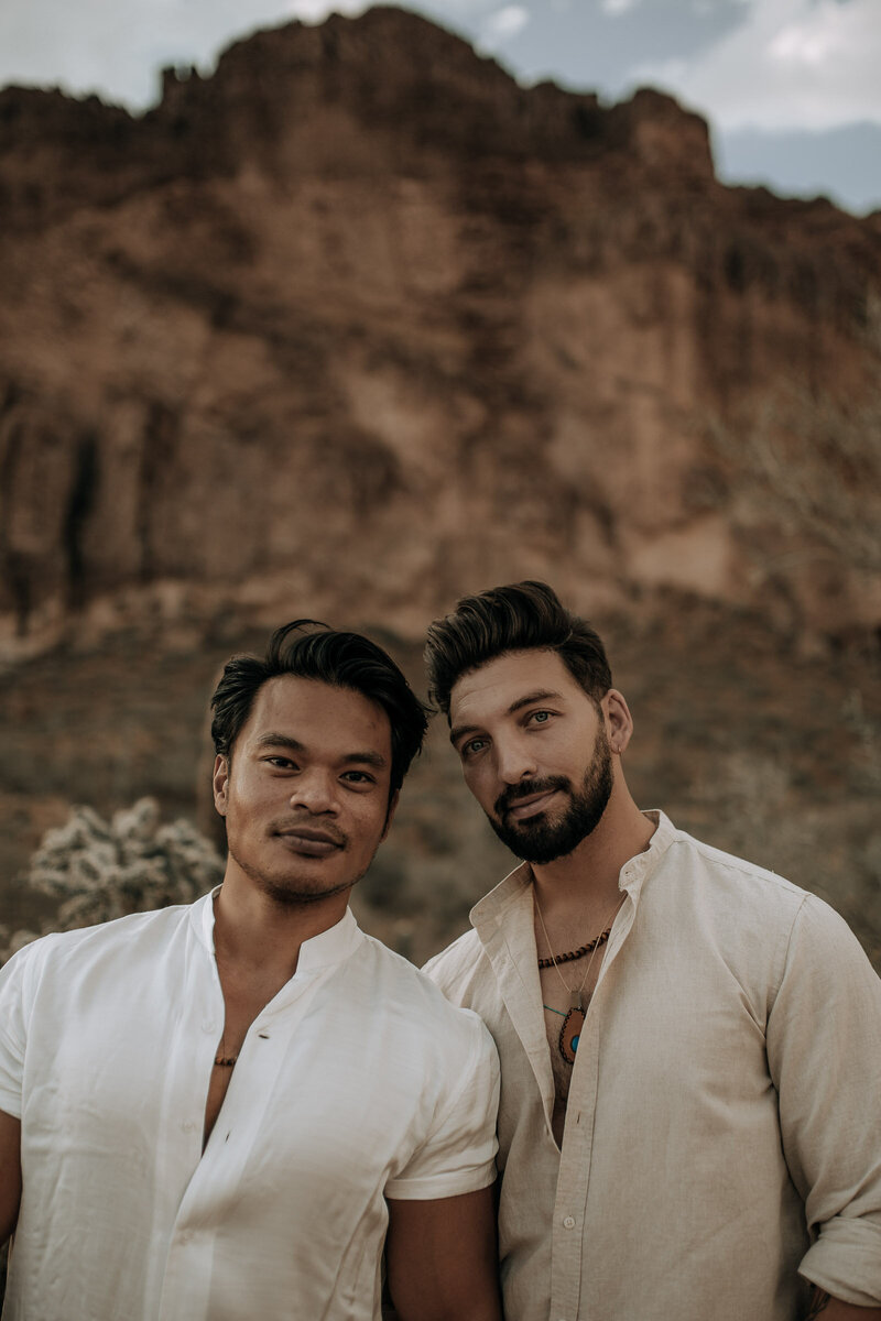 gay couple smizing at the camera in linen outfits with superstition mountain in the back ground