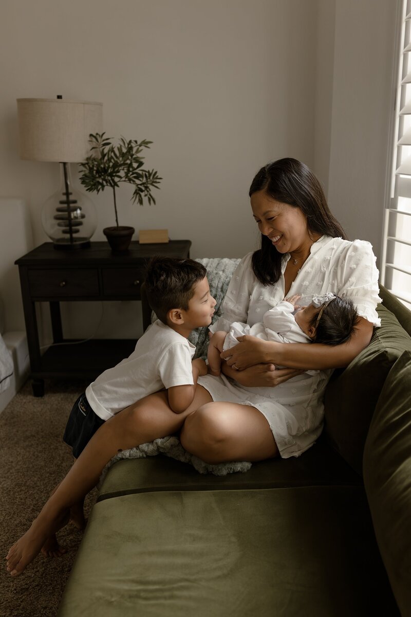 Mom holding a newborn in her arms, smiling at her other child