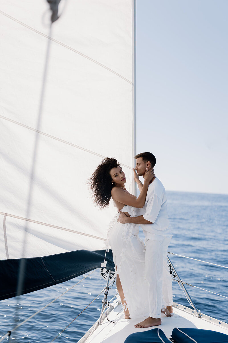Couple posing on the bow of a yacht while at sea.