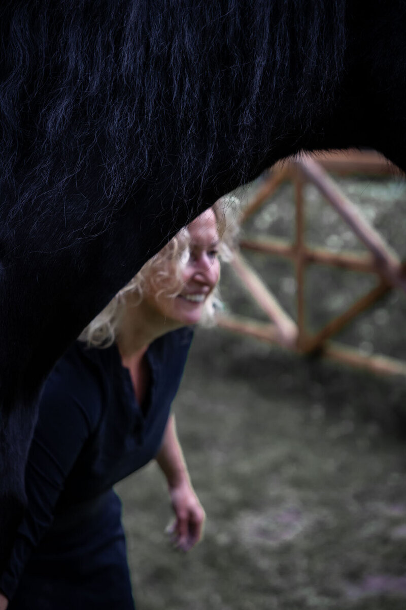 Monique kijkt onder hals van haar paard langs tijdens paardencoaching traject.