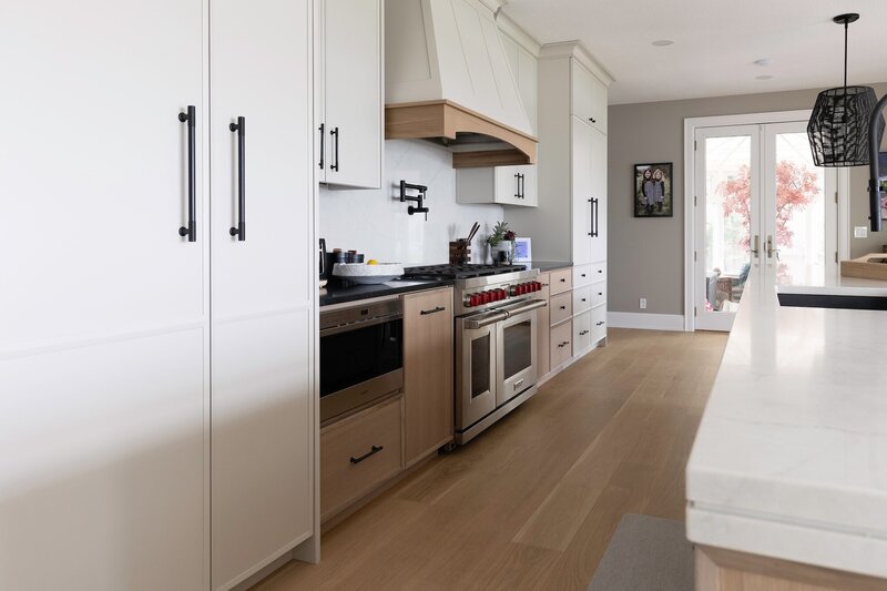 A mix of white and light wood cabinets with sleek black fixtures and white counter tops.