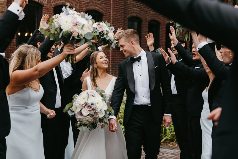 Bride and groom holding hands walking through a tunnel of the bridal party's arms