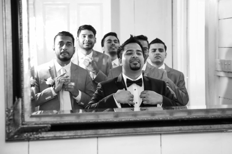 B+W image of groom and groomsmen adjust their suits in a mirror. Photo by Ross Photography, Trinidad, W.I..