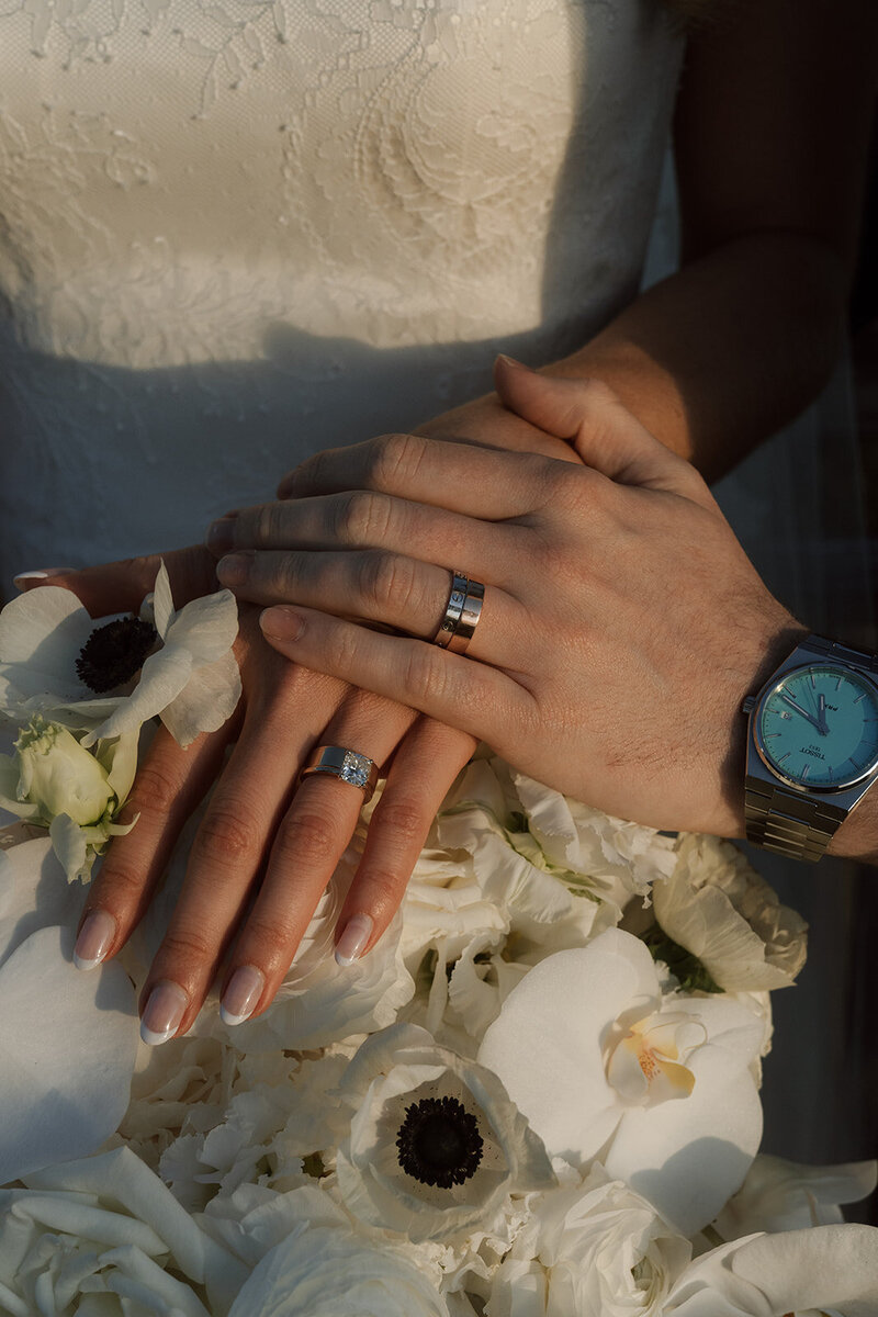 Bride and groom lay hands together over florals showing of rings