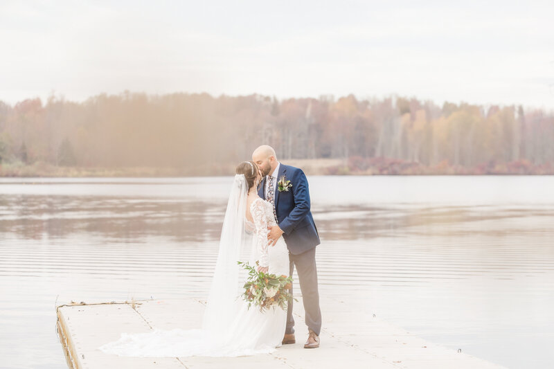 A newlywed couple kisses while standing on a lake dock for a Saginaw Wedding Photographer