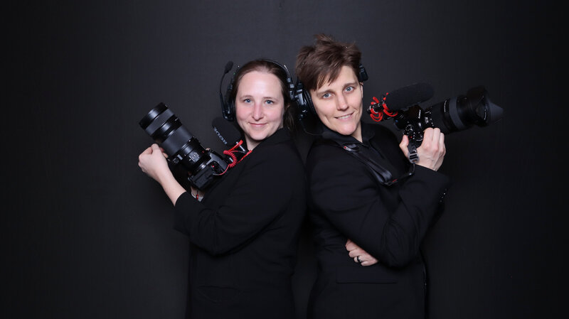 Two videographers standing back to back holding their cameras 