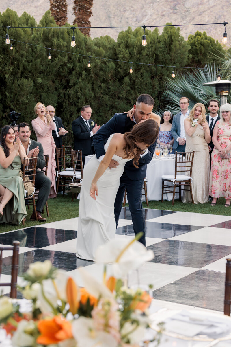 grooms dips the bride on a checkerd dance floor with orange and white florals in the foreground