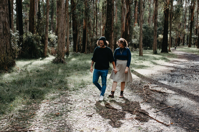 engaged couple walking through forest of tall trees together
