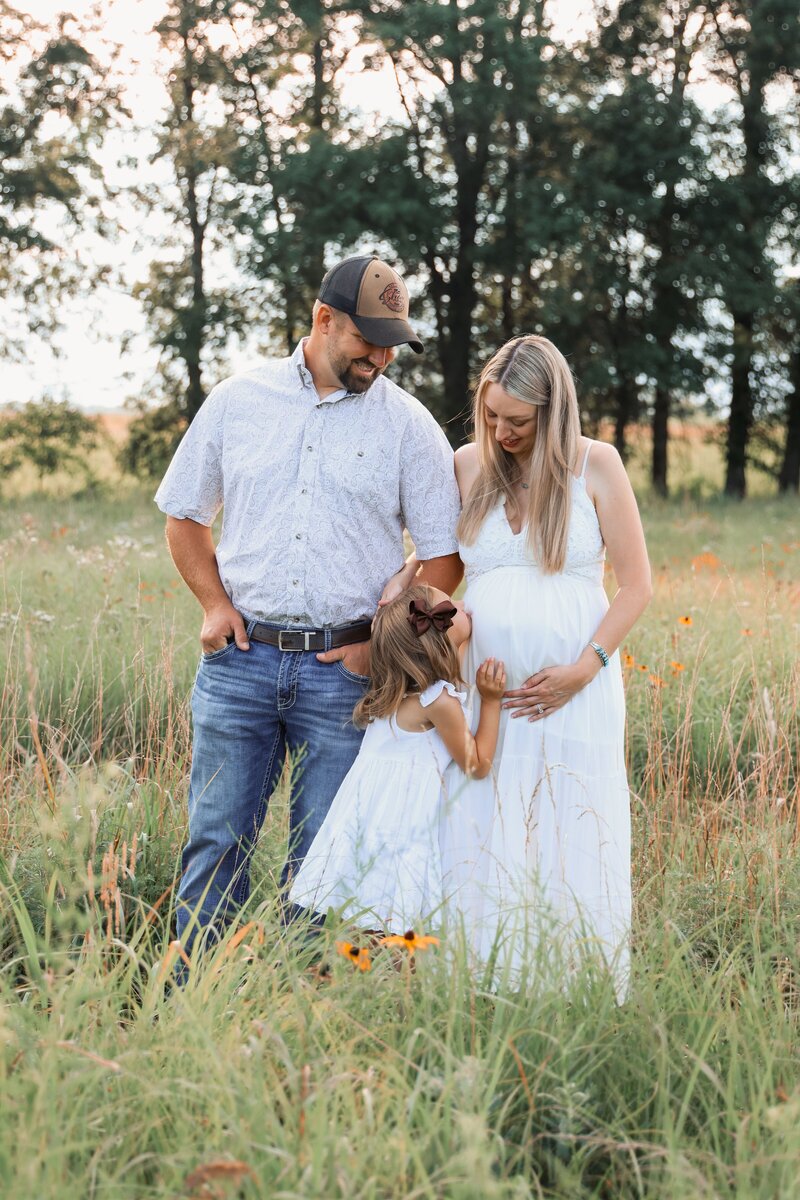 Family maternity photo where girl kisses mother's pregnant belly