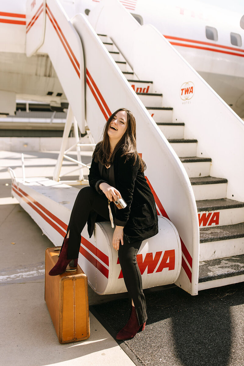 woman with suitcase and camera sits on tarmac stairs