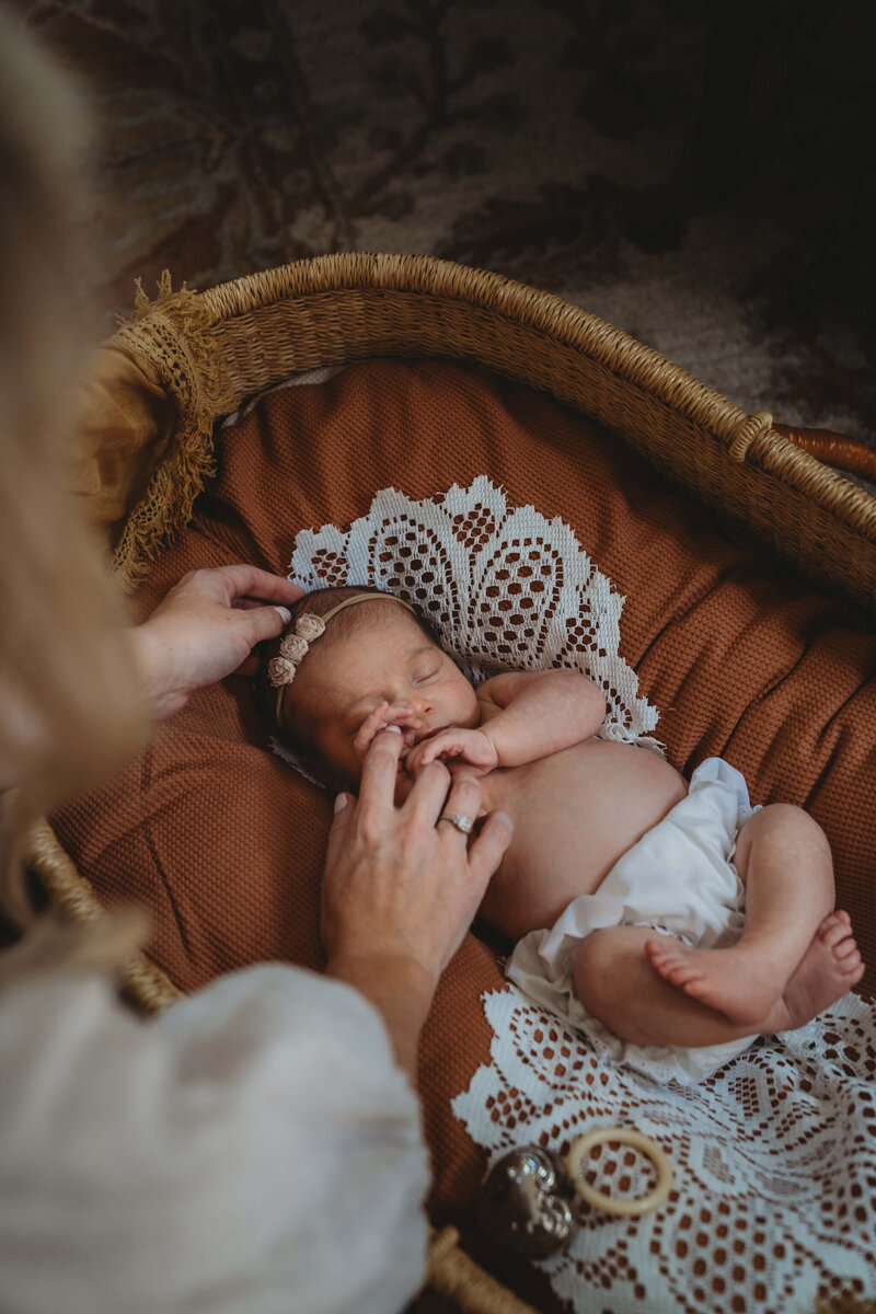 Newborn Lifestyle photography session of newborn baby in bassinet, mother holding finger.