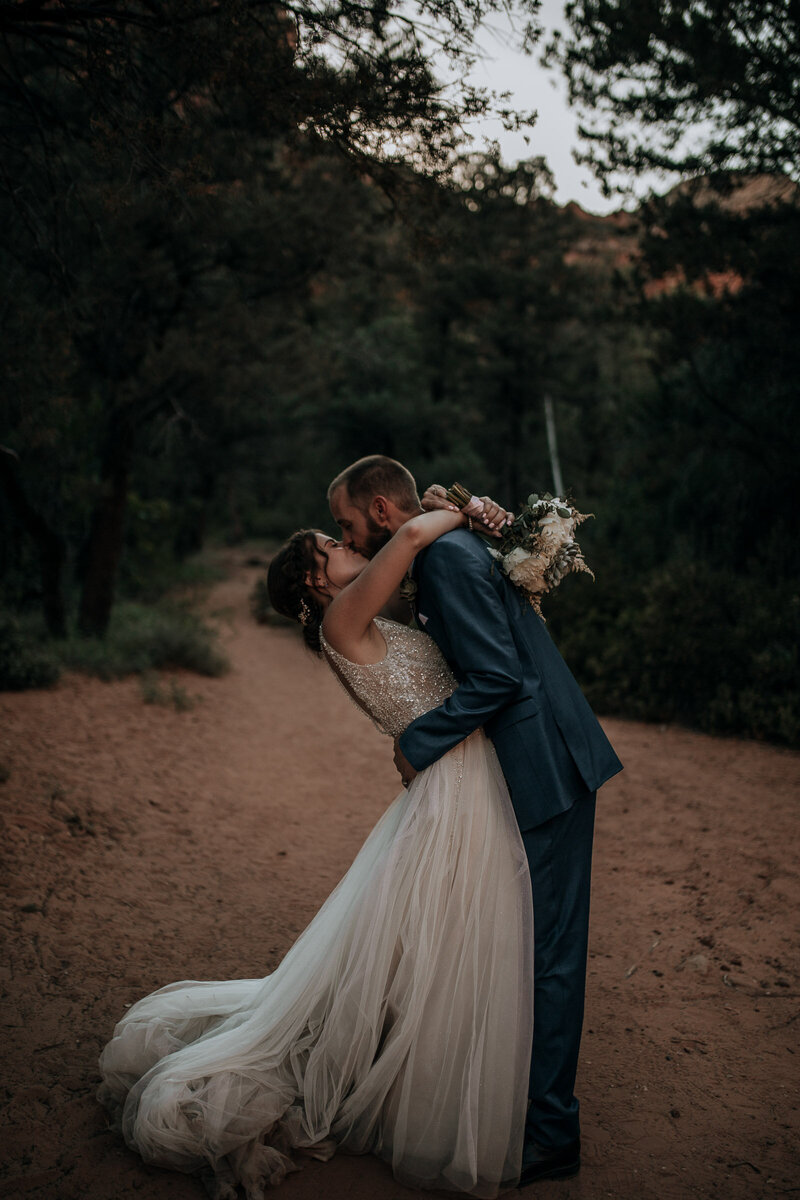 groom dipping and kissing bride in sedona canyon with red rocks and dirt in beautiful wedding dress