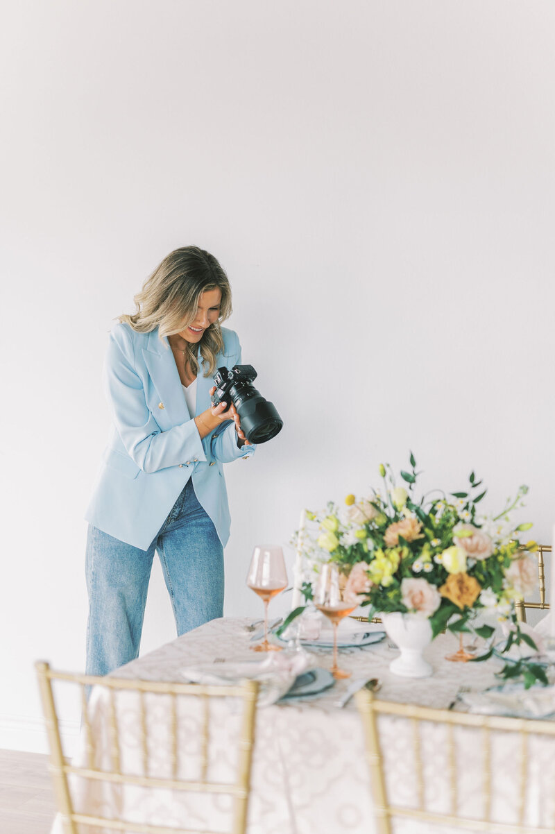 Headshot of Lindsey Kristian in a blue blazer and jeans taking a photo of a decorated tablescape