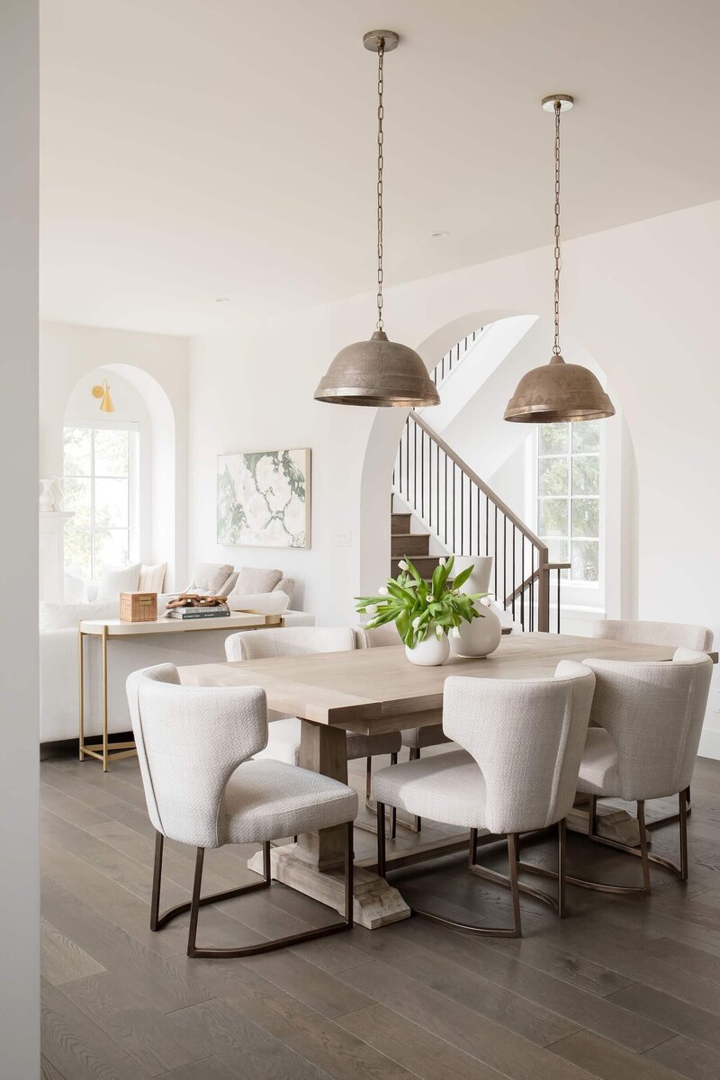 Wooden dining table with light upholstery and pendant lighting. 