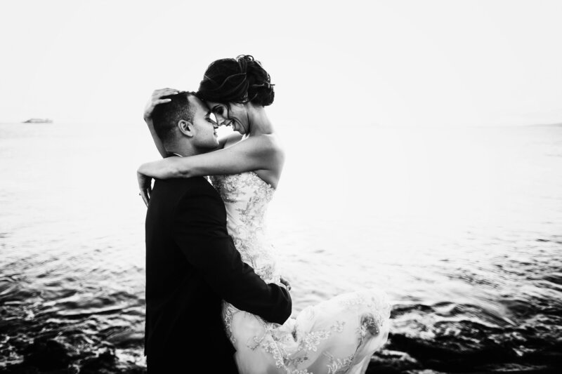 groom-holds-bride-up-before-ocean-waves