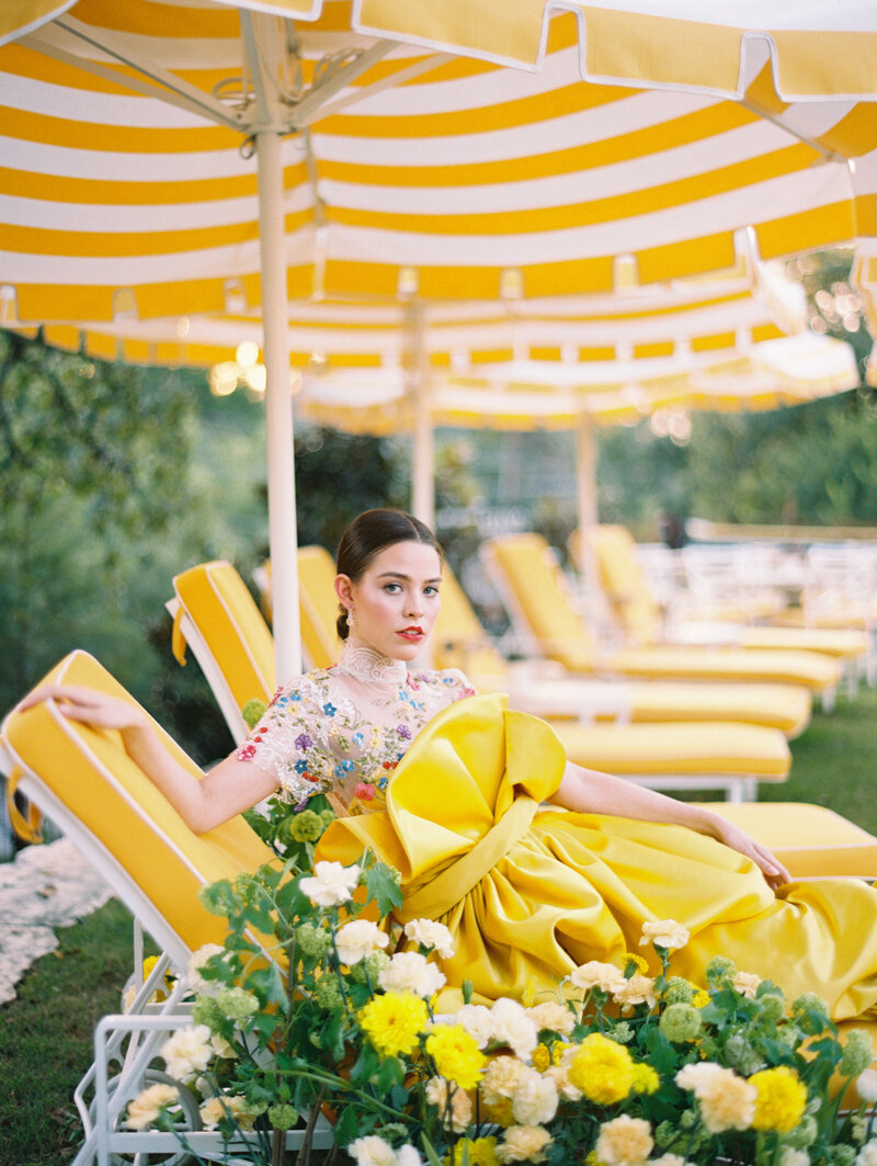 Model in yellow dress reclining on yellow pool chair