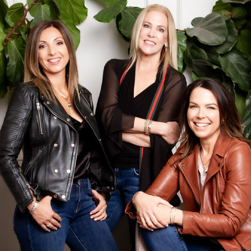 Group Branding Image Three Stories Jewelers three women entrepreneurs standing in front of white wall with green leaves while smiling