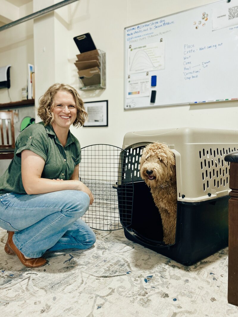 Woman kneeling in front of a dog in an open crate