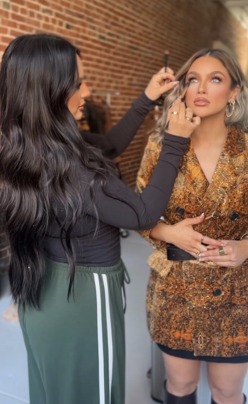 Pill shape image of a makeup artist putting makeup on someone.
