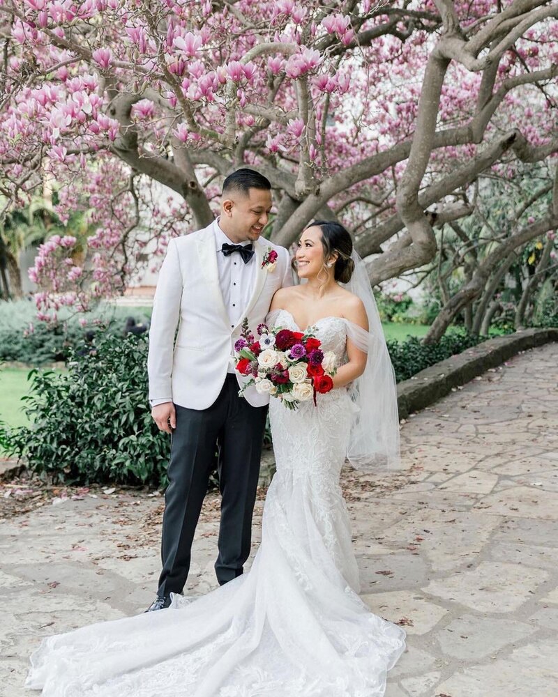 bride and groom stand beneath cherry blossom trees